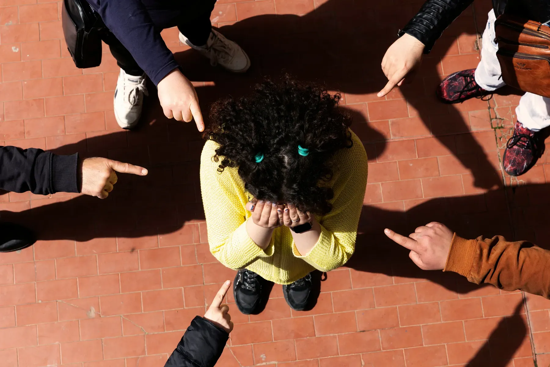 Teenage girl hiding her face in her hands, surrounded by several hands pointing fingers at her