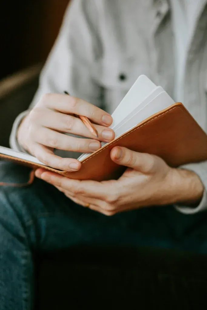 Hands holding an open small leather notebook and a pencil, blank white pages