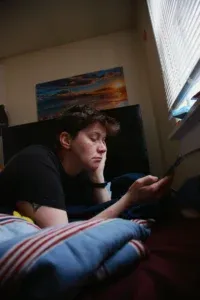 Adolescent allongé sur son lit, la tête appuyée sur sa main, en train de regarder l'écran de son téléphone