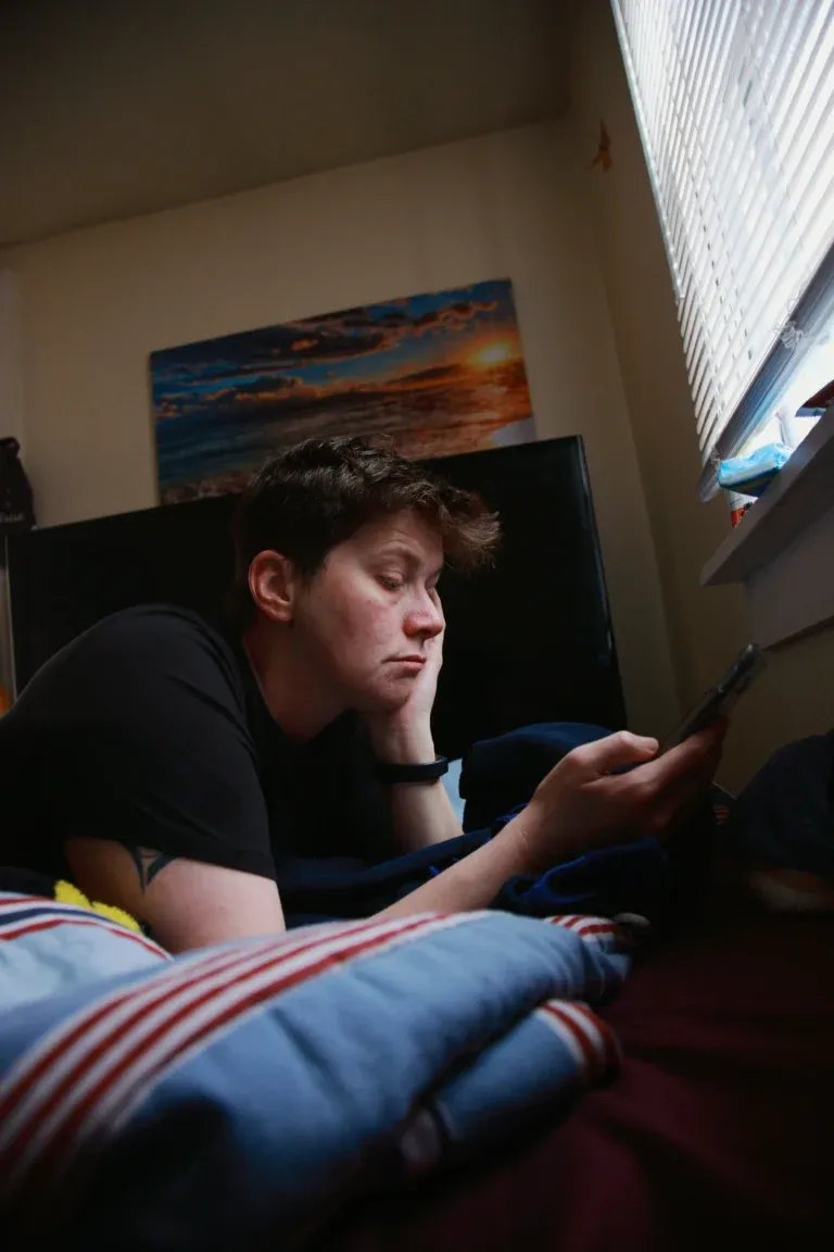 Adolescent allongé sur son lit, la tête appuyée sur sa main, en train de regarder l'écran de son téléphone