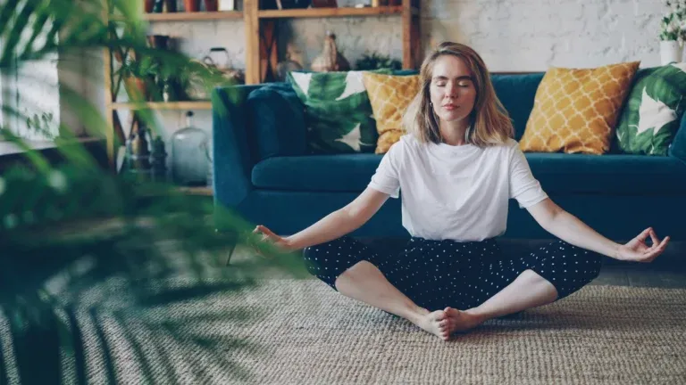 Personne assise en tailleur qui pratique la pleine conscience au salon