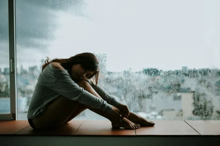 Personne assise seule près d'une fenêtre qui vit de la violence psychologique